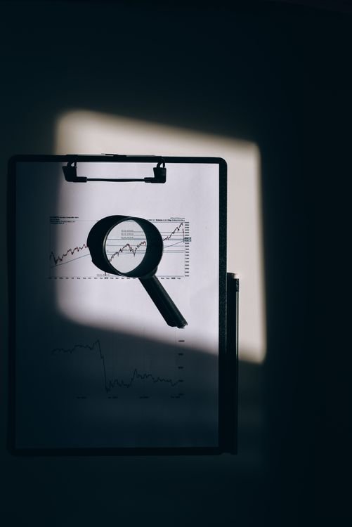 Black magnifying glass resting on a clipboard with charts, symbolising AI deep research