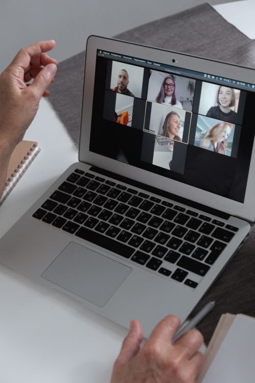 Hands at a laptop showing a group video call in a home office