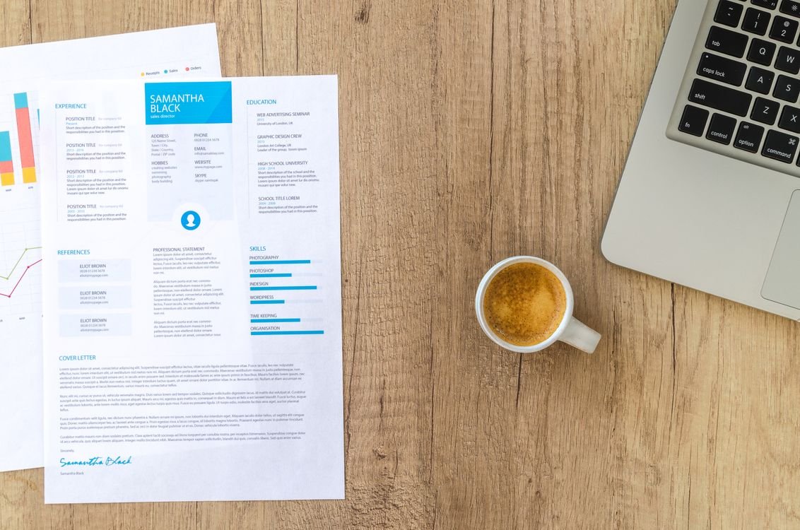 Top view of a wooden desk with a resume, coffee cup and laptop during a job application